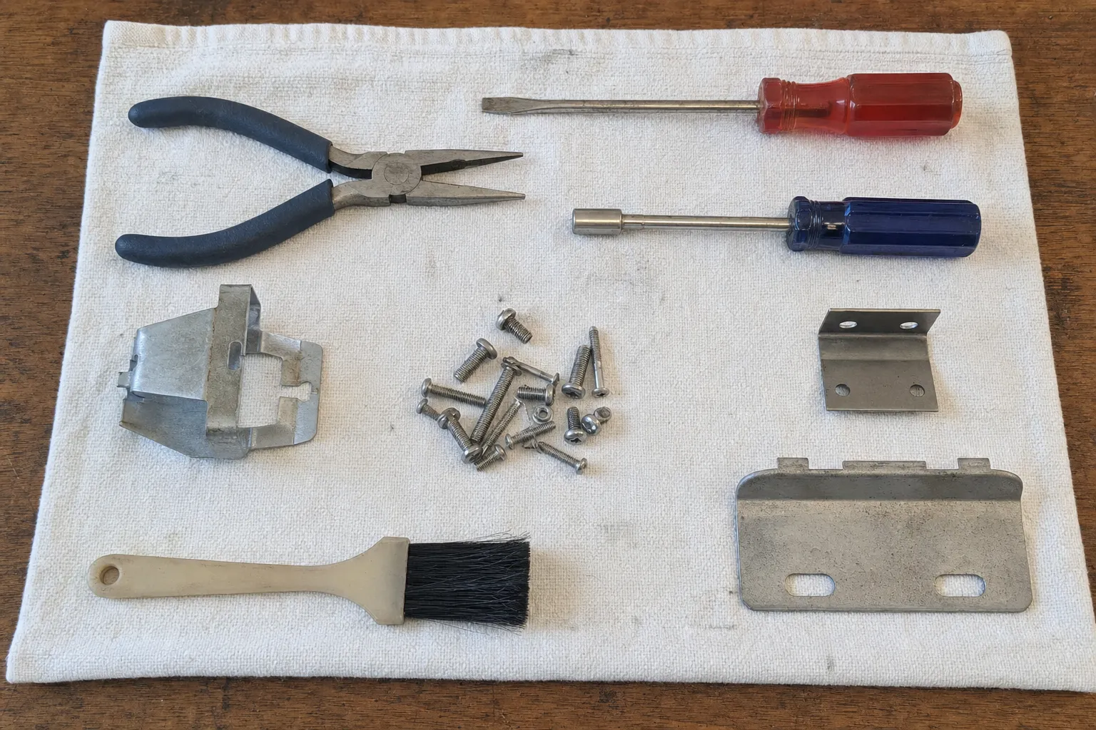 Oven door latch and hinge components laid out beside pliers, nut drivers and a soot brush
